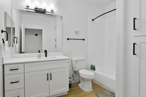 A modern bathroom with a white sink, mirror, and toilet. There is a shower area with a glass door and a towel rack. - TWO CozySuites Apartment DowntownChandler (Glendale)