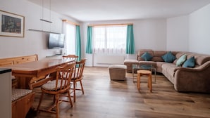 A modern living room with a wooden dining table, chairs, a sofa, and a TV. - Haus Sunneschy Whg. 202 by Interhome (Parpan)