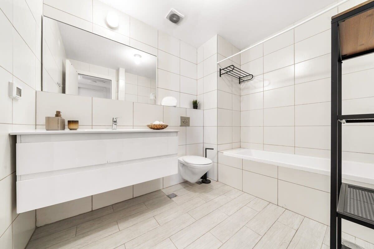 Une salle de bain moderne avec des carreaux blancs, un meuble-lavabo blanc, des toilettes et une baignoire.