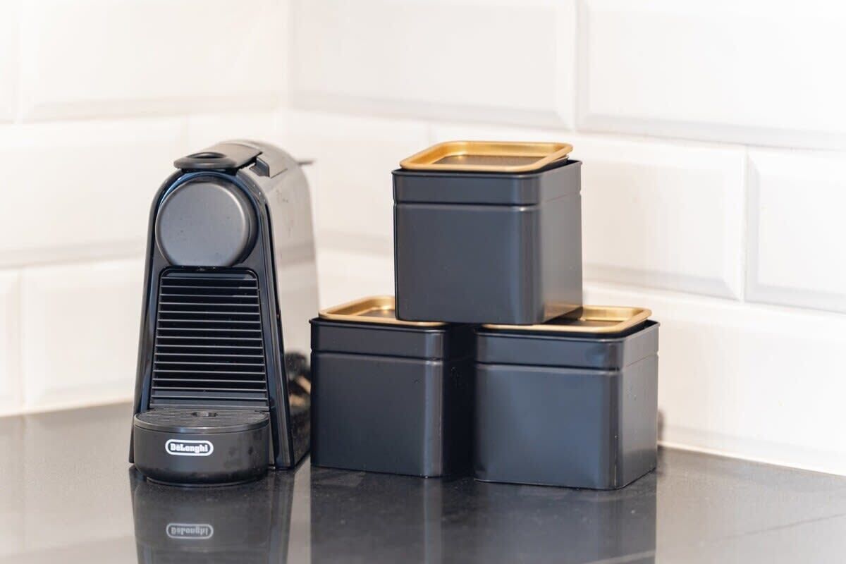 A kitchen with a black coffee maker and three black containers with gold lids.