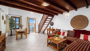 Un vaste salon agrémenté d’un escalier en bois, un coin repas avec une table et des chaises, et un espace salon confortable avec un canapé et des coussins.