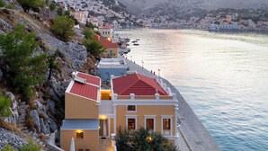 Un hôtel situé sur la côte, avec un bâtiment à toit rouge, une promenade pavée longeant la mer et une vue sur la ville en arrière-plan.