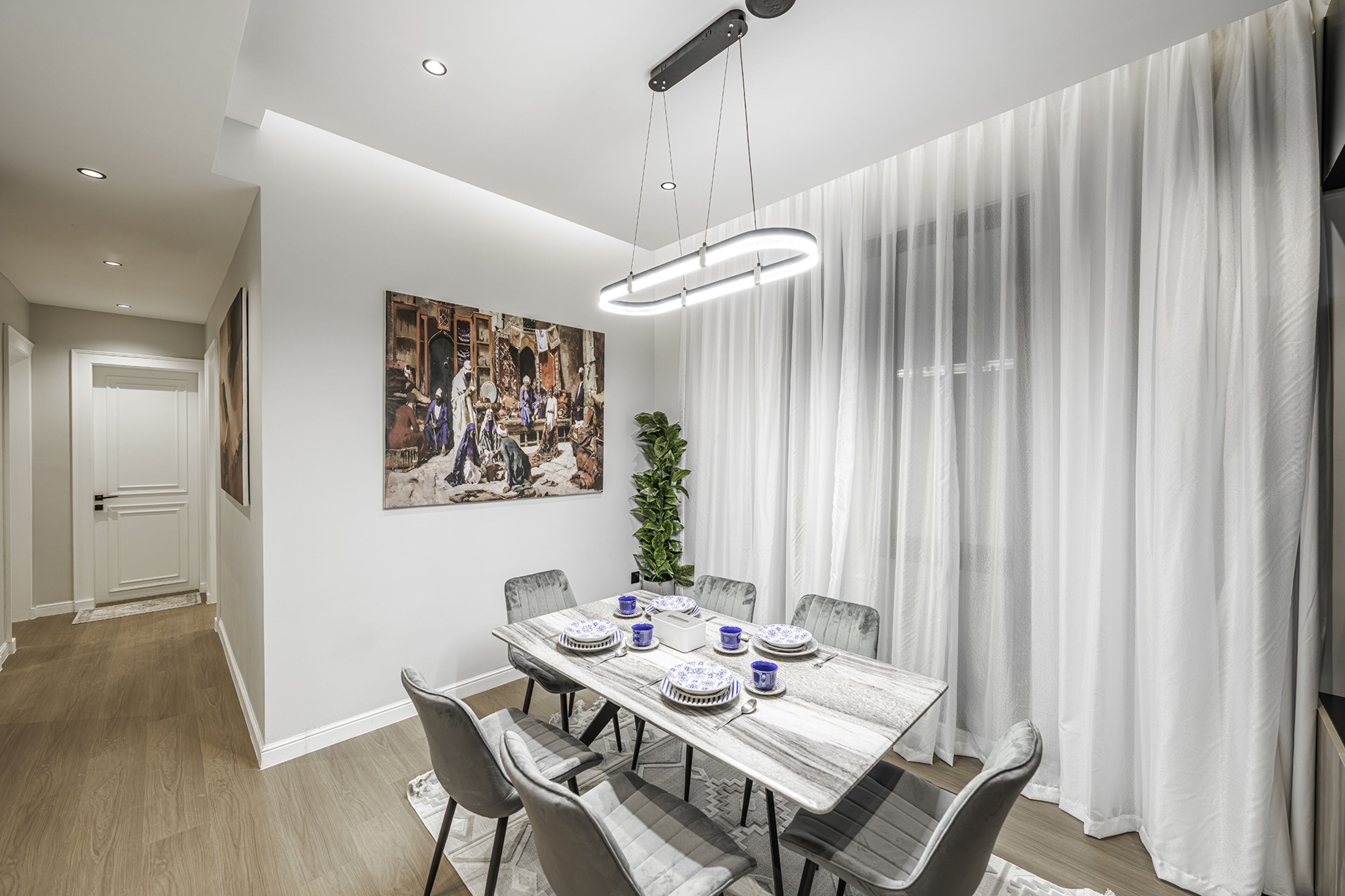 A dining area with a marble table, grey chairs, and a painting on the wall.