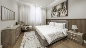 A modern bedroom with a large bed, a nightstand, a chair, a dresser, and a painting on the wall. - Mabaat - Al Malqa - 543 (Riyadh)