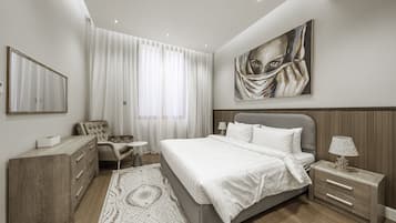 A modern bedroom with a large bed, a nightstand, a chair, a dresser, and a painting on the wall.