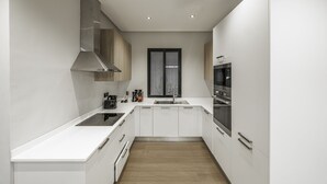 A modern kitchen with white cabinetry, a stainless steel range hood, a built-in oven, and a window above the sink. - Mabaat - Al Malqa - 543 (Riyadh)