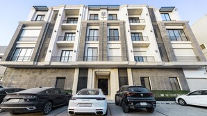 A multi-story building with a central entrance, balconies, and a parking area with several cars. - Mabaat - Al Malqa - 543 (Riyadh)