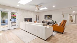 Un salon moderne avec un canapé blanc, un fauteuil marron, une cheminée et un ventilateur de plafond.