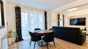 A modern living room with a round dining table, black chairs, a black sofa, and a TV mounted on the wall. - Résidence Champenoise Lancelot Rouyer (Épernay)