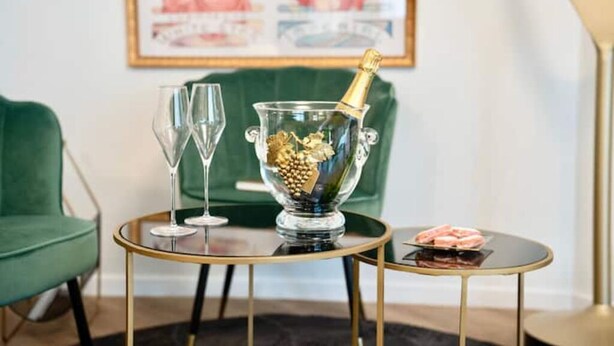 A room with a green sofa, a glass table with a gold base, a glass bowl with a bottle of champagne, and two empty wine glasses. - Résidence Champenoise Lancelot Rouyer (Épernay)