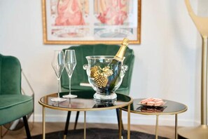 A room with a green sofa, a glass table with a gold base, a glass bowl with a bottle of champagne, and two empty wine glasses. - Résidence Champenoise Lancelot Rouyer (Épernay)