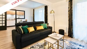 A modern living room with a black sofa, gold accents, and a view into the kitchen. - Résidence Champenoise Lancelot Rouyer (Épernay)