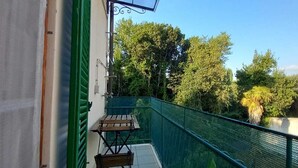 A balcony with a wooden table and chairs, a green railing, and a view of trees and buildings. - Sosia Palace, Pisa (Pisa)