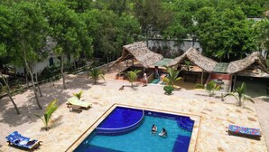 Piscina com interior azul, rodeada por espreguiçadeiras e uma área arenosa.