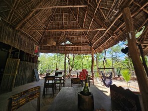 An outdoor seating area with thatched roof, wooden furniture, and hanging hammocks.