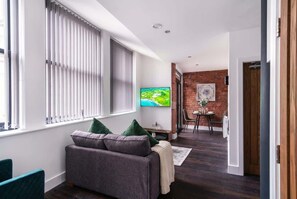 A modern living room with a sofa, a television, and a brick wall. - Modern Central Liverpool Apartment with Balcony (Liverpool)