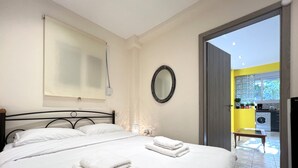 Een hotelkamer met een bed, nachtkastje, spiegel en uitzicht op de keuken en het balkon.