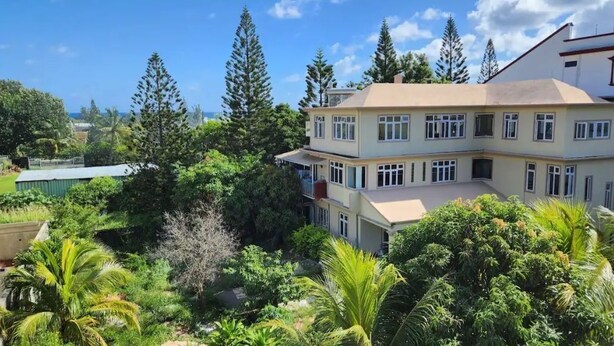 A multi-story building with a flat roof, surrounded by dense greenery and tall trees. - Villa Orchidee Un Havre de Paix (Pamplemousses)