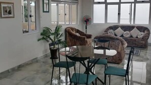 A spacious living area with a round glass-top table surrounded by four chairs, a brown armchair, and a patterned sofa. - Villa Orchidee Un Havre de Paix (Pamplemousses)