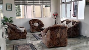 A spacious living room with three brown armchairs, a coffee table, and a floor lamp. Large windows allow natural light to fill the room. - Villa Orchidee Un Havre de Paix (Pamplemousses)