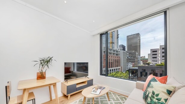 A modern living room with a large window, a TV, a wooden table, a sofa, and a plant. - Studio With City Views (Cape Town)