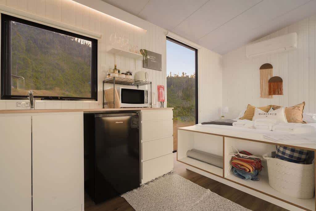 A modern kitchen with white cabinetry, a built-in microwave, and a refrigerator. There is a large window providing a view of the outdoors.