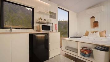 A modern kitchen with white cabinetry, a built-in microwave, and a refrigerator. There is a large window providing a view of the outdoors.