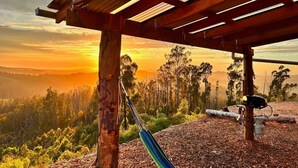Un hamac sous une pergola en bois, agrémenté d’un panneau indiquant « POINT DE VUE », surplombant un paysage boisé au coucher du soleil.