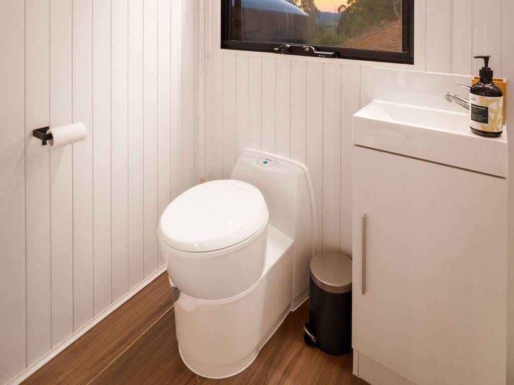 A modern bathroom with a white toilet, a small trash bin, and a window above the sink.