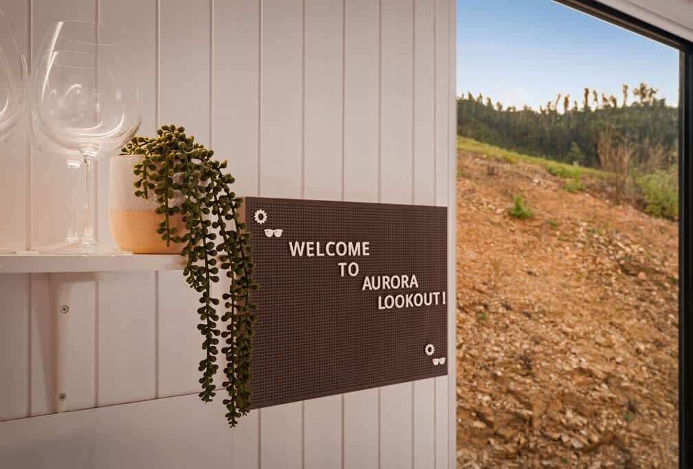 Velkomstskilt for Aurora Lookout med en plante og glas på en hvid væg.