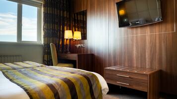A hotel room with a bed, a desk with a lamp, a TV, and a window.