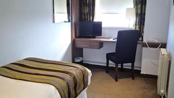 Habitación de hotel con cama, escritorio con computadora, silla, teléfono y ventana con cortinas.