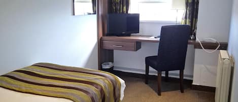 Une chambre d’hôtel avec un lit, un bureau équipé d’un ordinateur, une chaise, un téléphone et une fenêtre avec des rideaux.