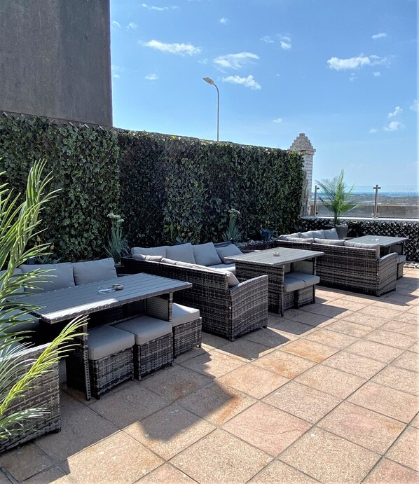 An outdoor seating area with wicker furniture and a tiled floor, overlooking a scenic view. - Hotel Ambassadeur (St. Clement)