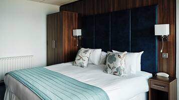 A hotel room with a large bed, a wooden wardrobe, a bedside table with a phone, and a wall-mounted light fixture.