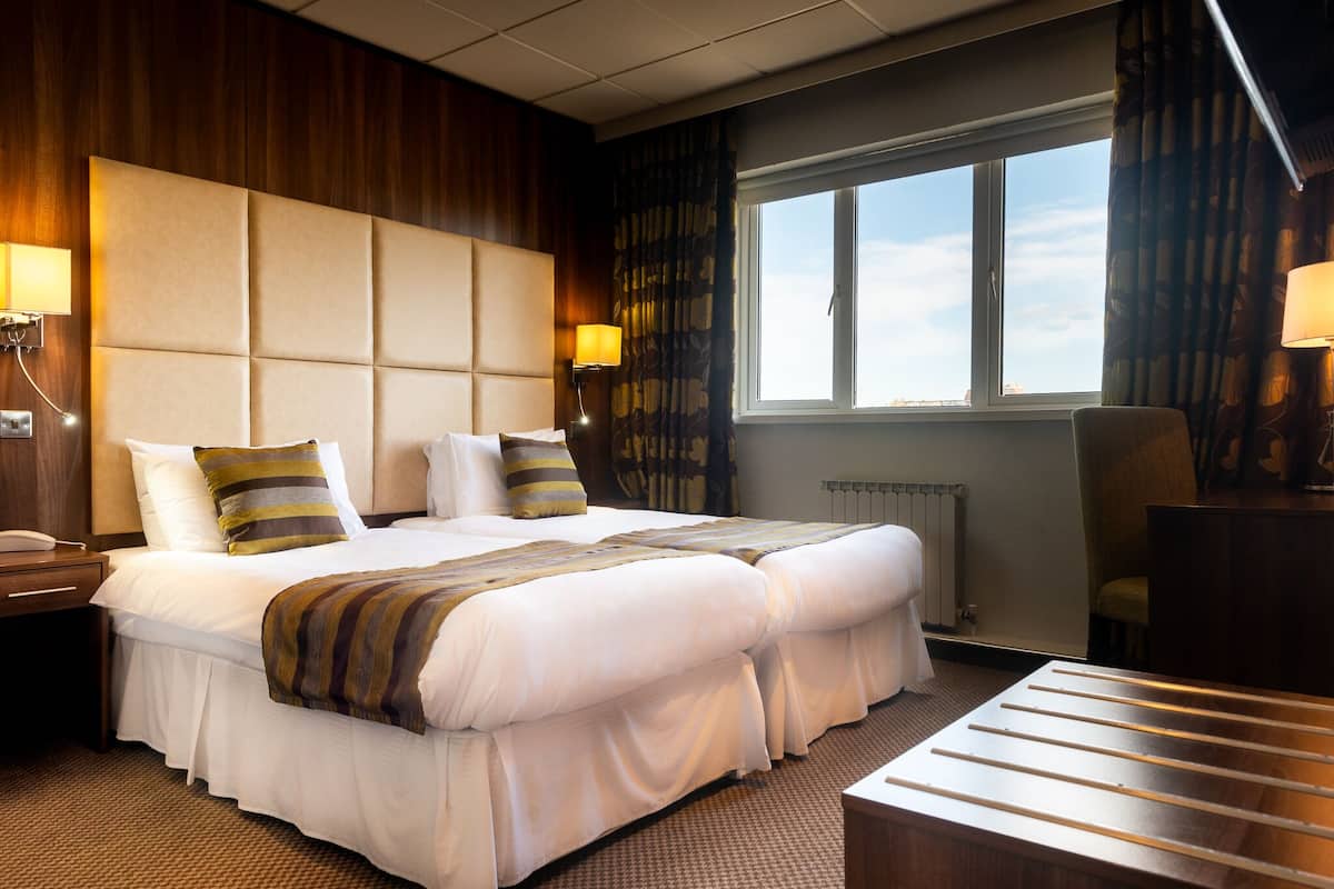 A hotel room with a large bed, two bedside tables, a chair, a window with curtains, and a radiator.