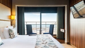 A hotel room with a bed, two chairs, a small table, a TV, and a view of the sea. - Hotel Ambassadeur (St. Clement)