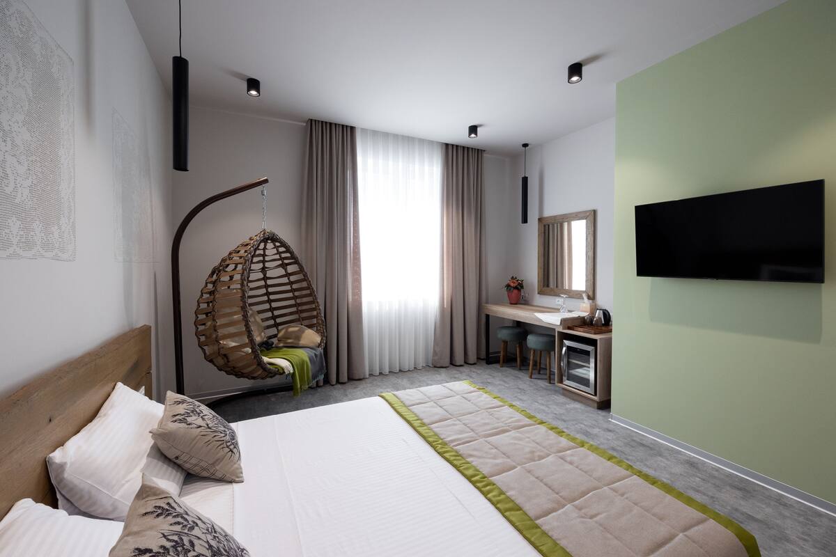 A modern hotel room with a large bed, a desk, a hanging chair, and a flat-screen TV.