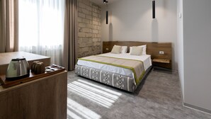 A hotel room with a bed, a wooden desk with a kettle, a brick wall, and a window with curtains. - ECODOR HOTEL (Orhei)