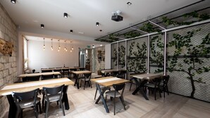 A modern dining area with wooden tables and chairs, a stone wall, and a green vine-covered partition. - ECODOR HOTEL (Orhei)