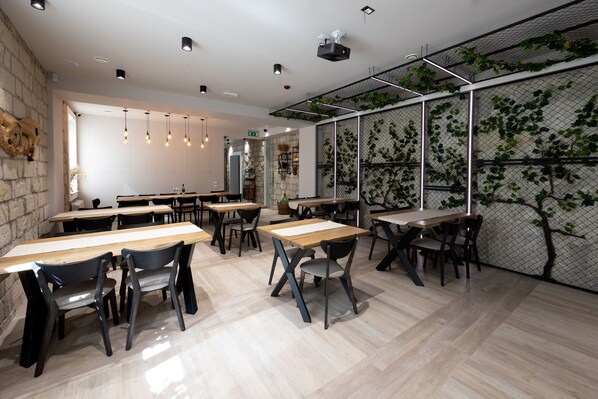 A modern dining area with wooden tables and chairs, a stone wall, and a green vine-covered partition.