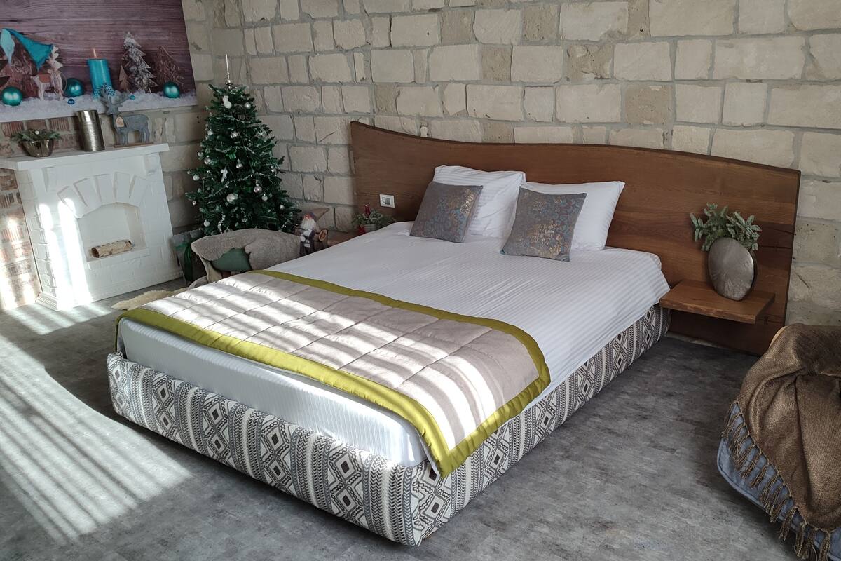 A bedroom with a large bed, a nightstand, a small Christmas tree, and a fireplace.