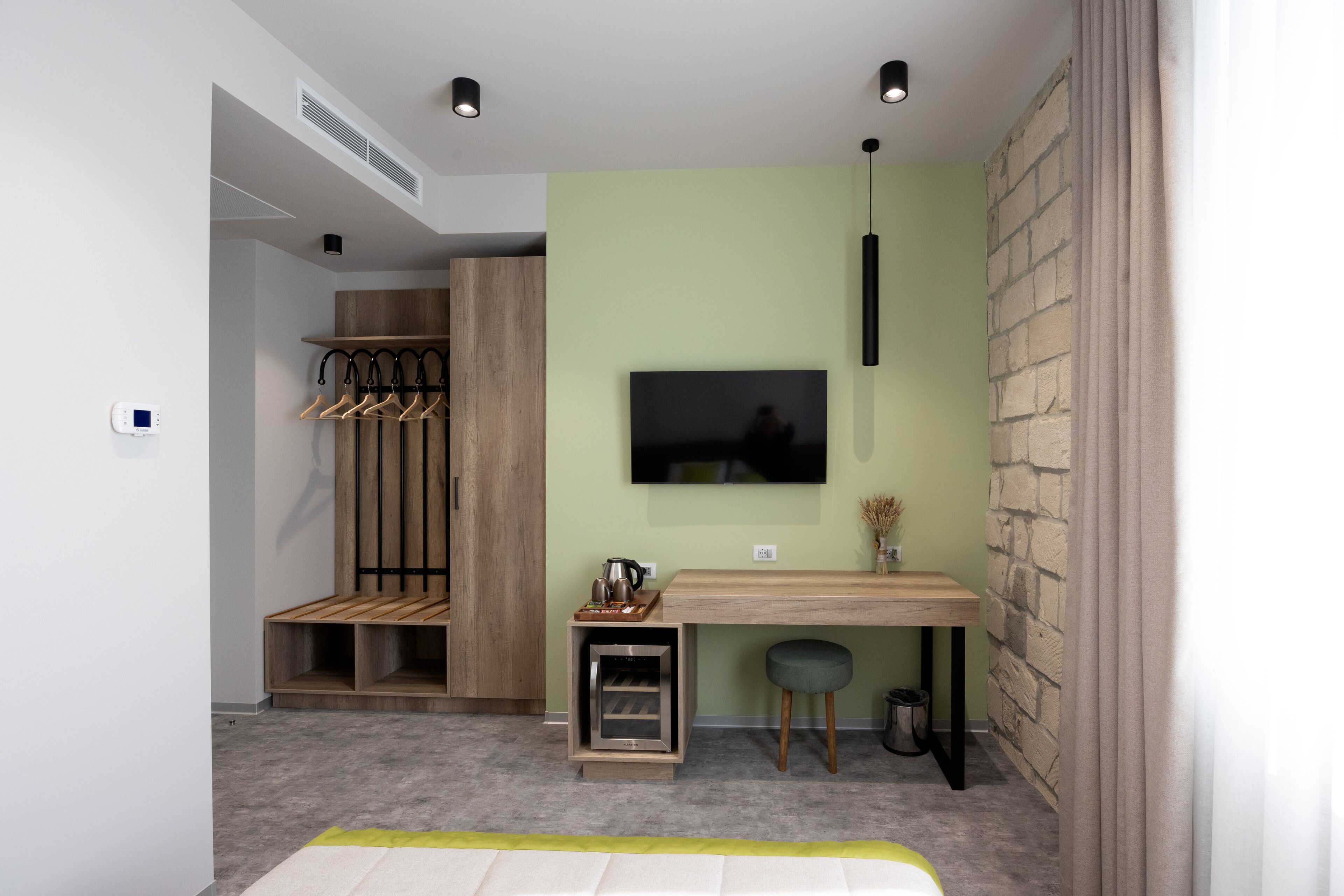Une chambre moderne dotée d’un bureau en bois, d’un téléviseur fixé au mur et d’un coin salon avec un banc et un tabouret.
