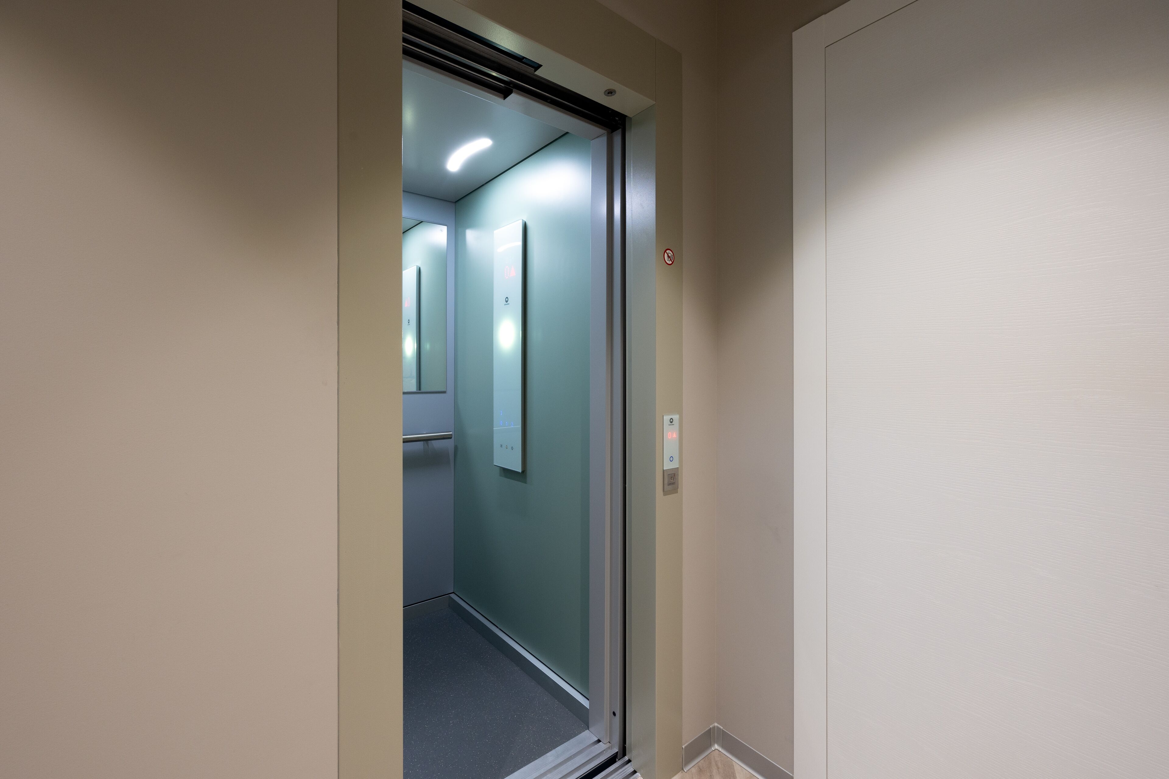 En smal hall med en glasdörr som leder in till ett rum, en ljusströmbrytare och en dörrklocka.