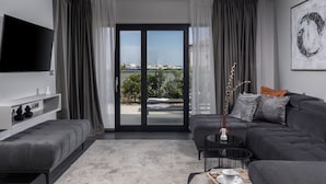 Ein modernes Wohnzimmer mit grauem Sofa, einem Flachbildfernseher, einem Couchtisch und Blick auf eine Marina durch große Glasüren.
