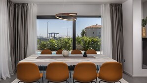 Ein moderner Essbereich mit einem großen Tisch, sechs orangenen Stühlen und Blick auf eine Marina durch große Fenster.