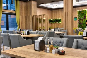 A modern hotel restaurant with wooden paneling, grey upholstered chairs, and a wooden table with a paper dispenser, salt and pepper shakers, and a small plant.