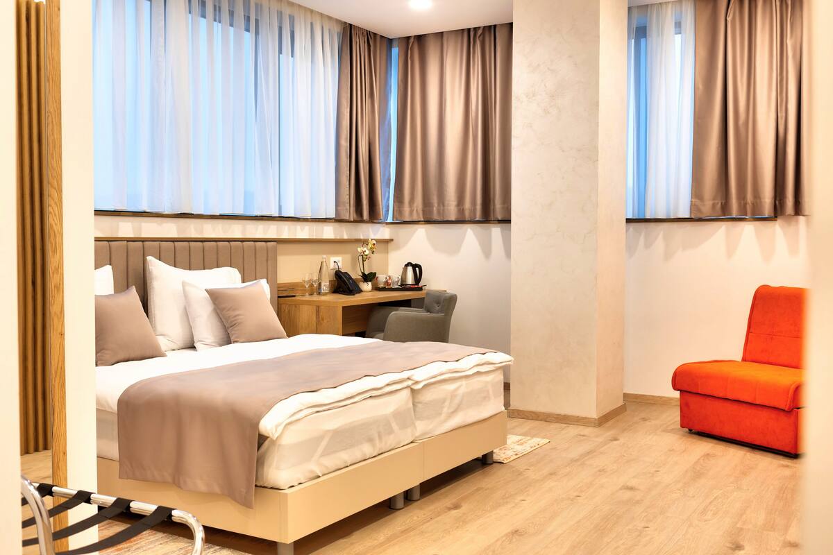 A modern bedroom with a bed, bedside table, chair, and a desk with a chair.