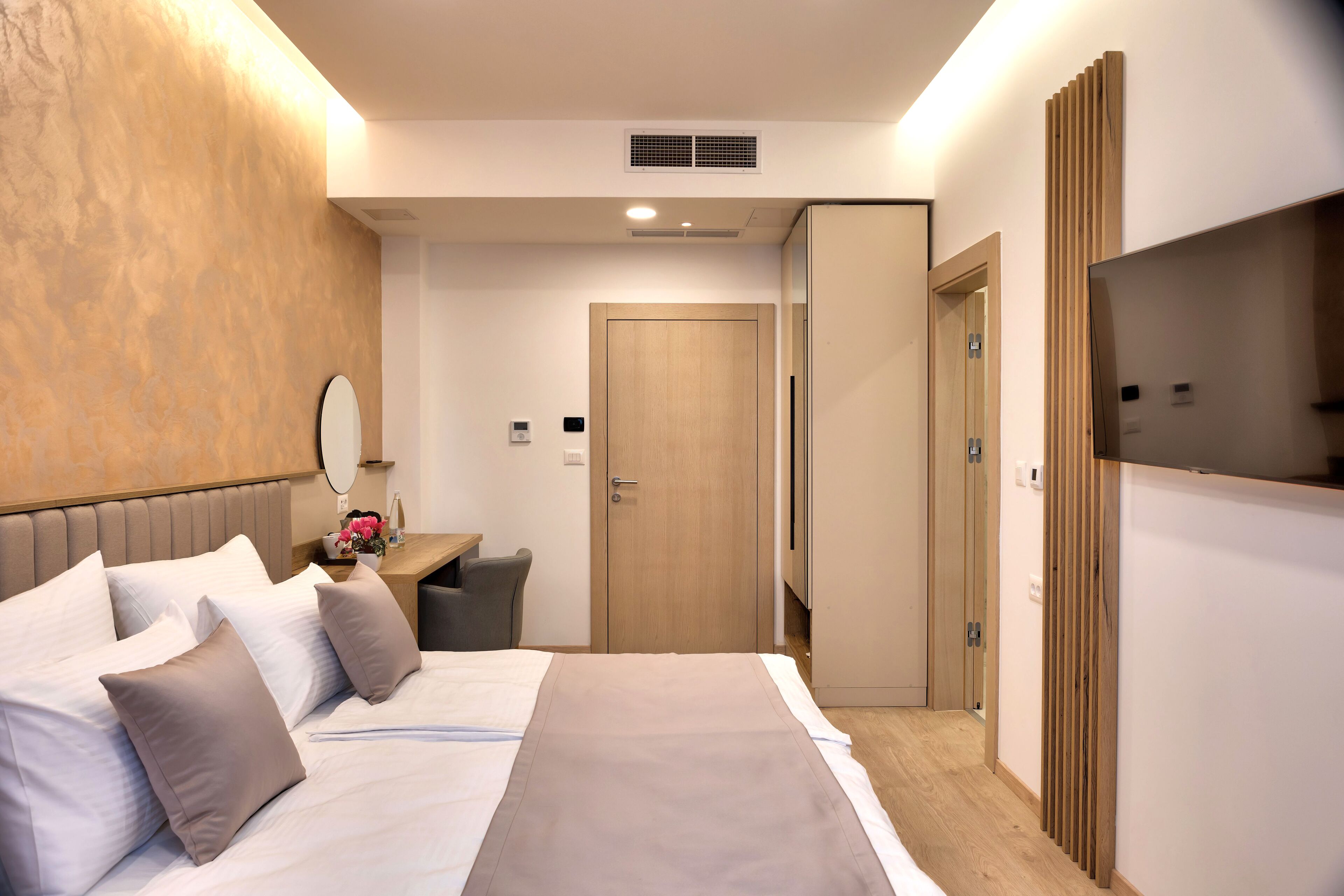 A hotel room with a bed, bedside table, mirror, and a TV.