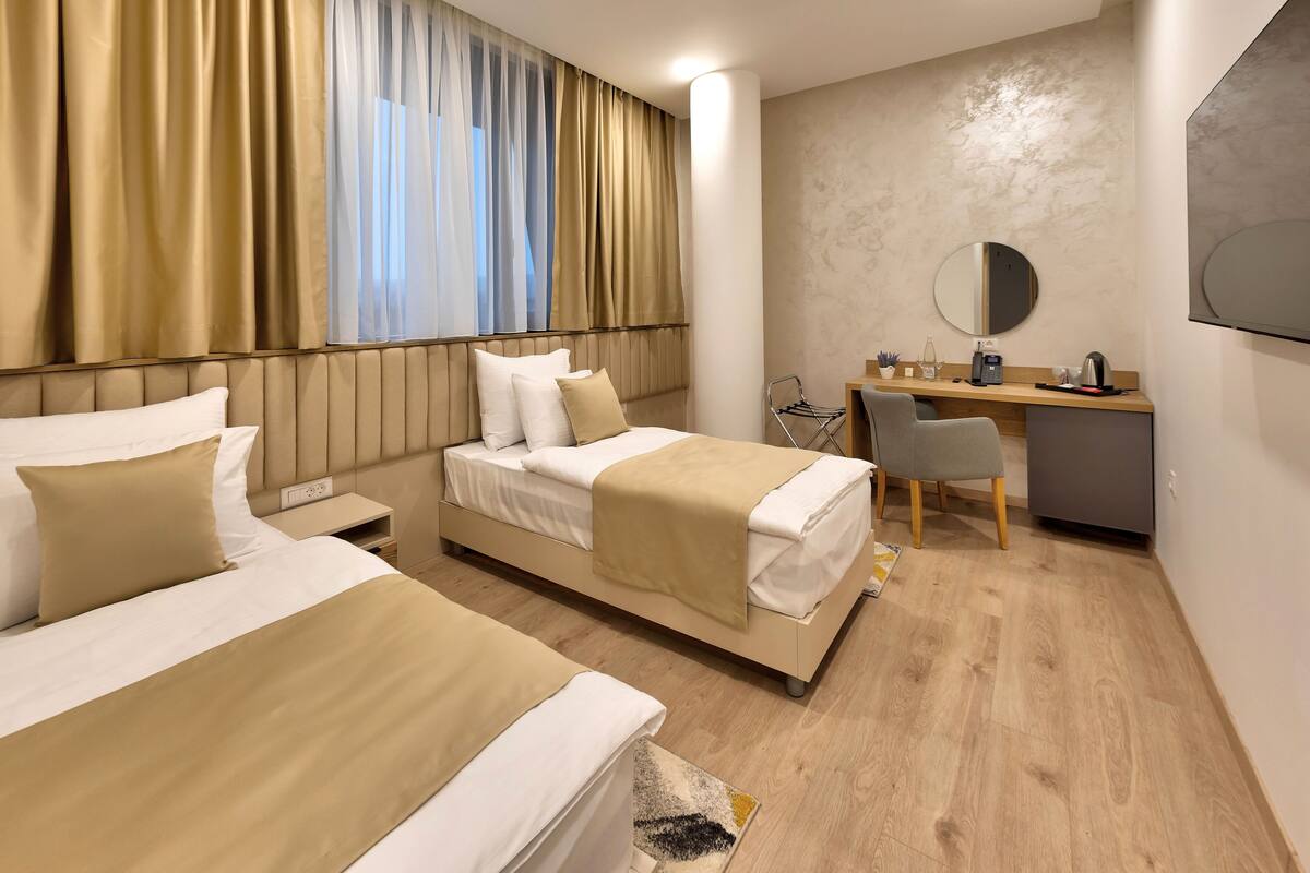 A hotel room with two beds, a desk, a chair, a mirror, and a TV.